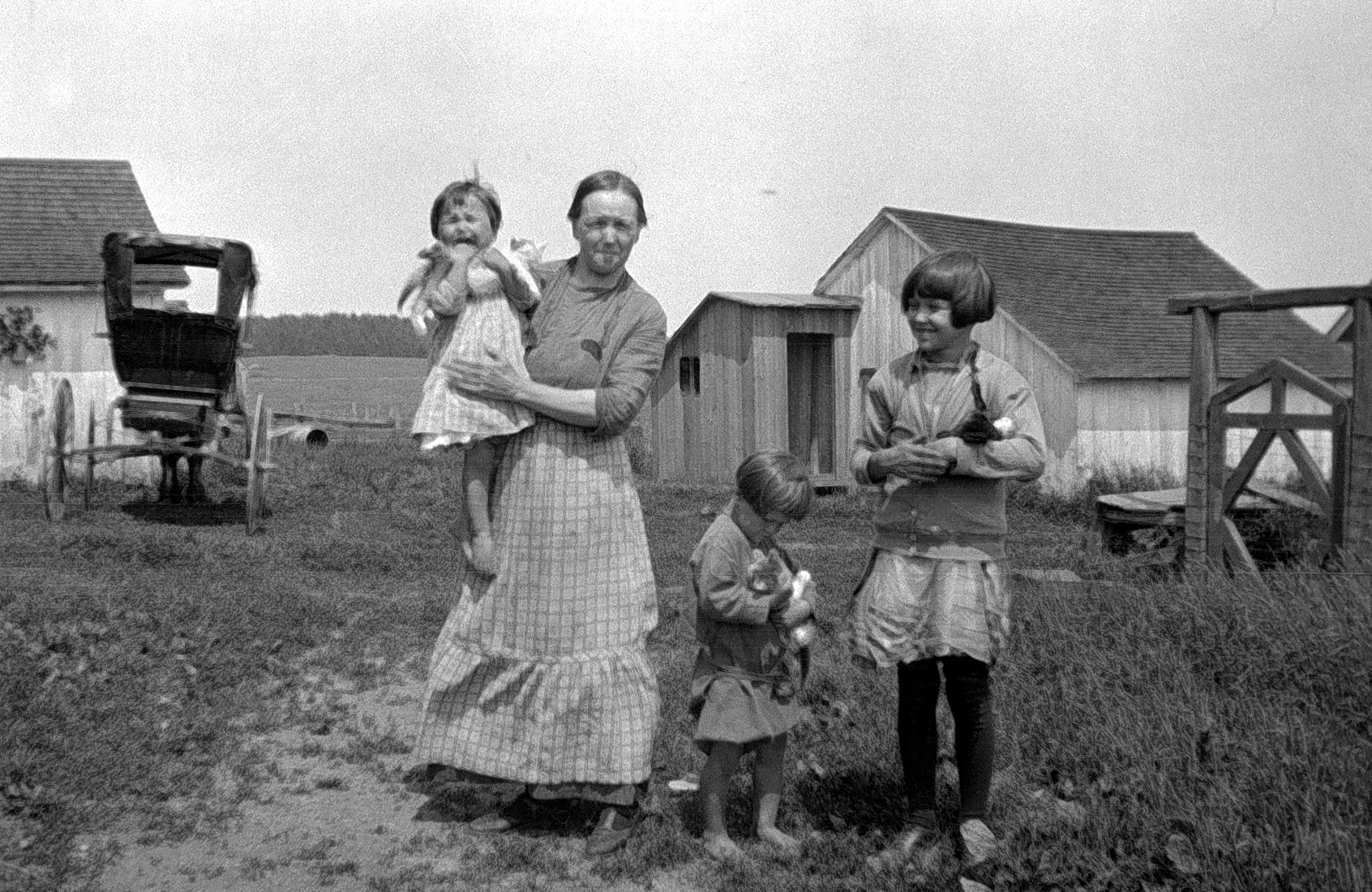 Mary April sur le terrain de la ferme, avec ses trois enfants chacun tenant un chat dans ses bras.
