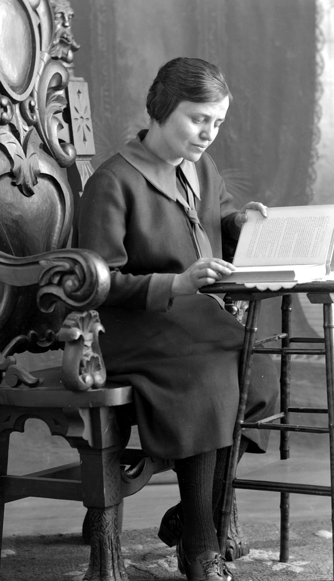 Autoportrait de Marie-Alice Dumont âgée d'environ 40 ans dans son studio, assise sur une grande chaise en bois et lisant un livre.