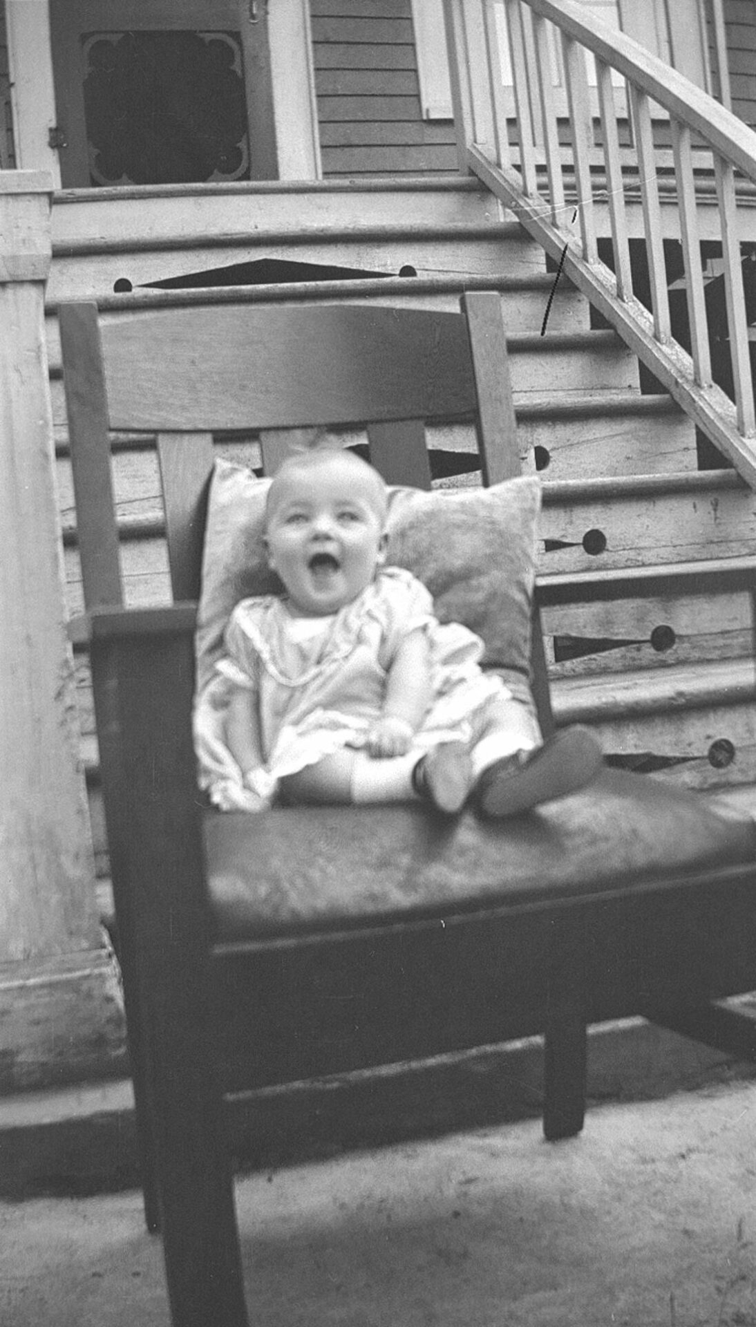 Un bébé souriant placé sur un fauteuil, à l'extérieur, devant les escaliers du studio Dumont.