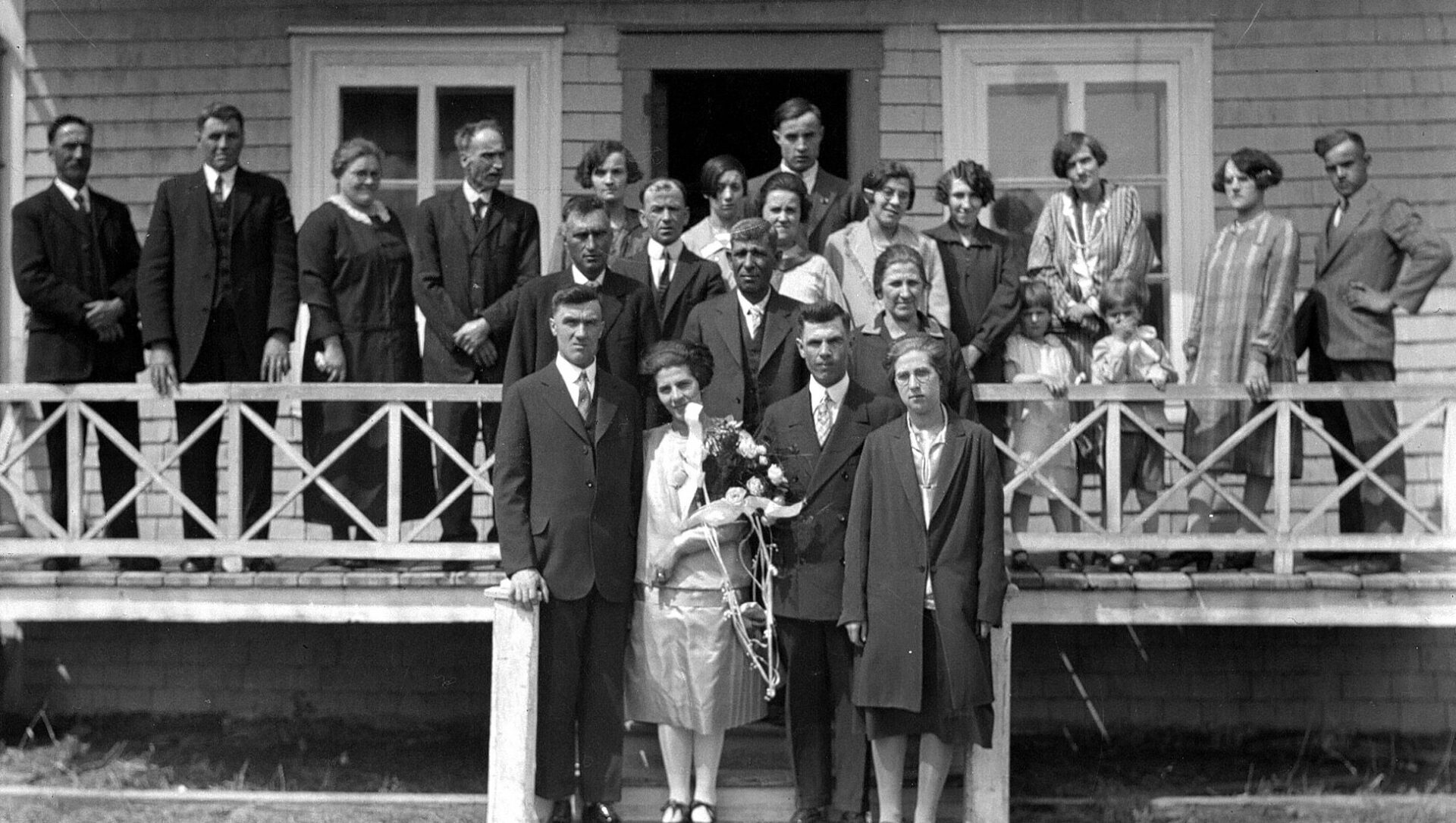 Groupe d'une vingtaine de personnes debout sur la galerie d'une maison lors d'un mariage.