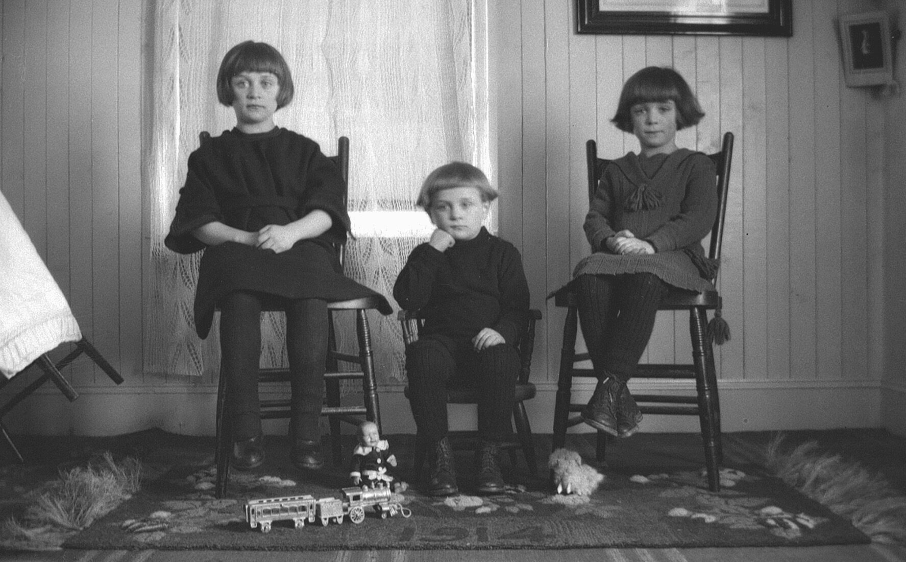 Portrait de deux jeunes filles et d'un petit garçon assis des chaises en bois dans un environnement domestique.