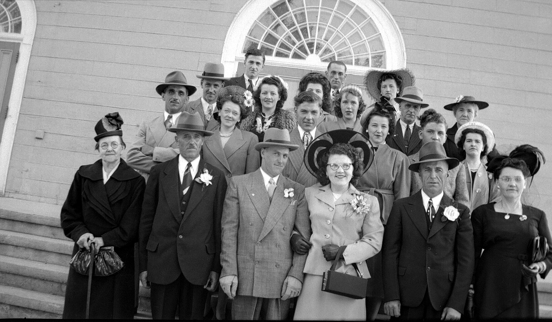 Un groupe de 21 personnes posées sur le perron d'une église à l'occasion d'un mariage.