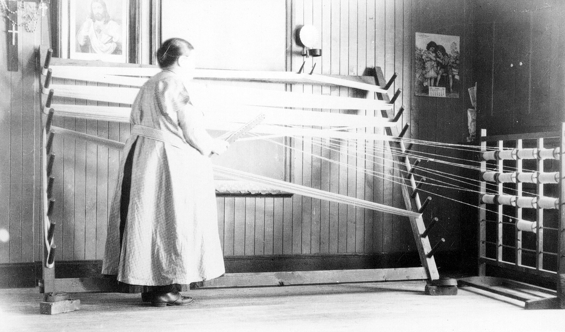 Marie Pelletier debout et travaillant à l'ourdissoir dans un environnement domestique.