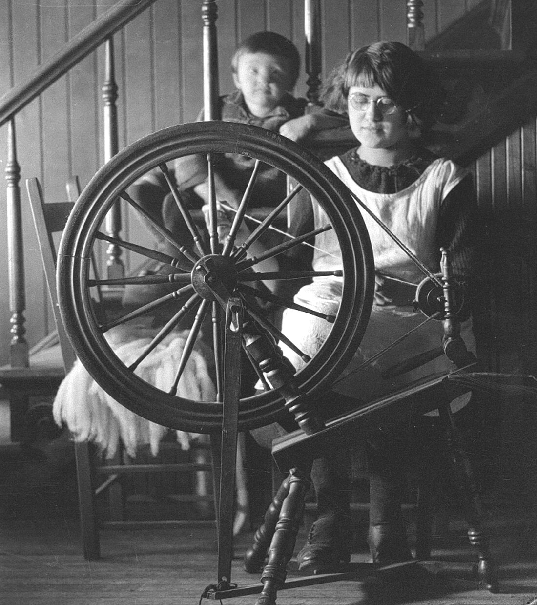 Elizabeth Dumont âgée d'environ 18 ans au rouet sous le regard de son neveu Origène Dumont âgé d'environ trois ans.