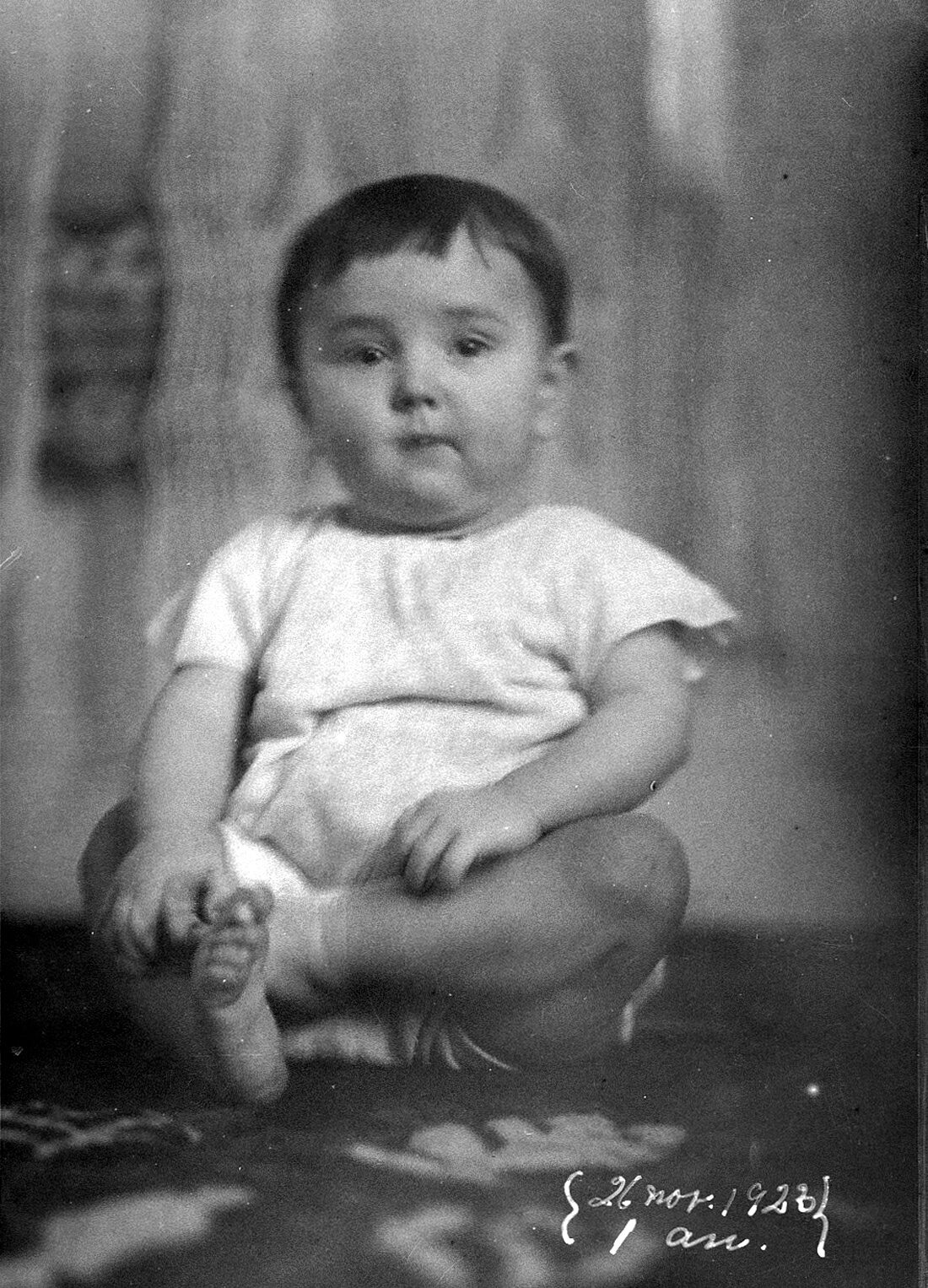 Portrait d'Origène Dumont âgé d'un an assis les jambes croisées sur un tapis dans un décor domestique.