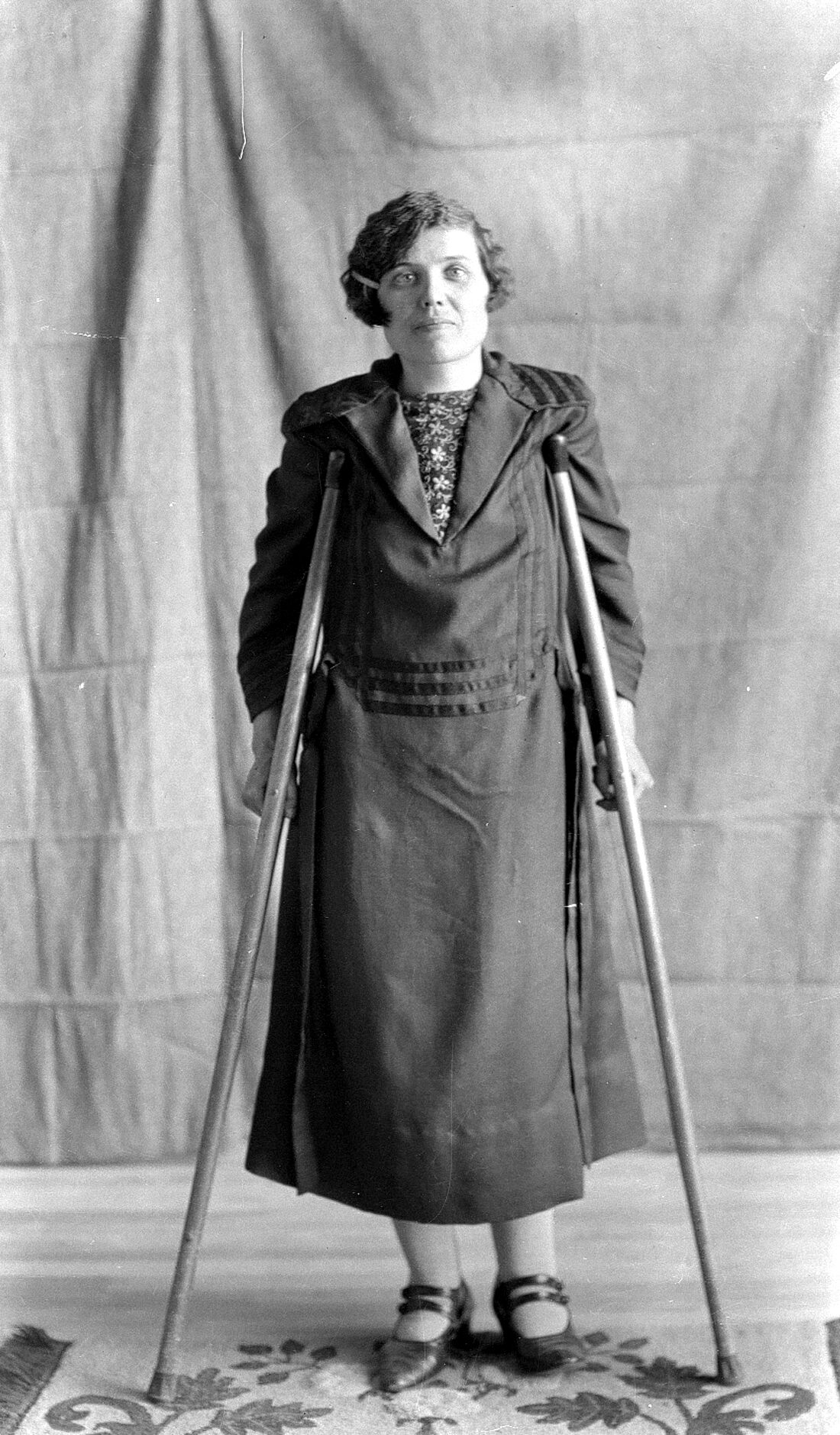 Portrait de studio de Marie-Louise Dumont âgée d'environ 30 ans, en béquilles, dans un décor dépouillé.