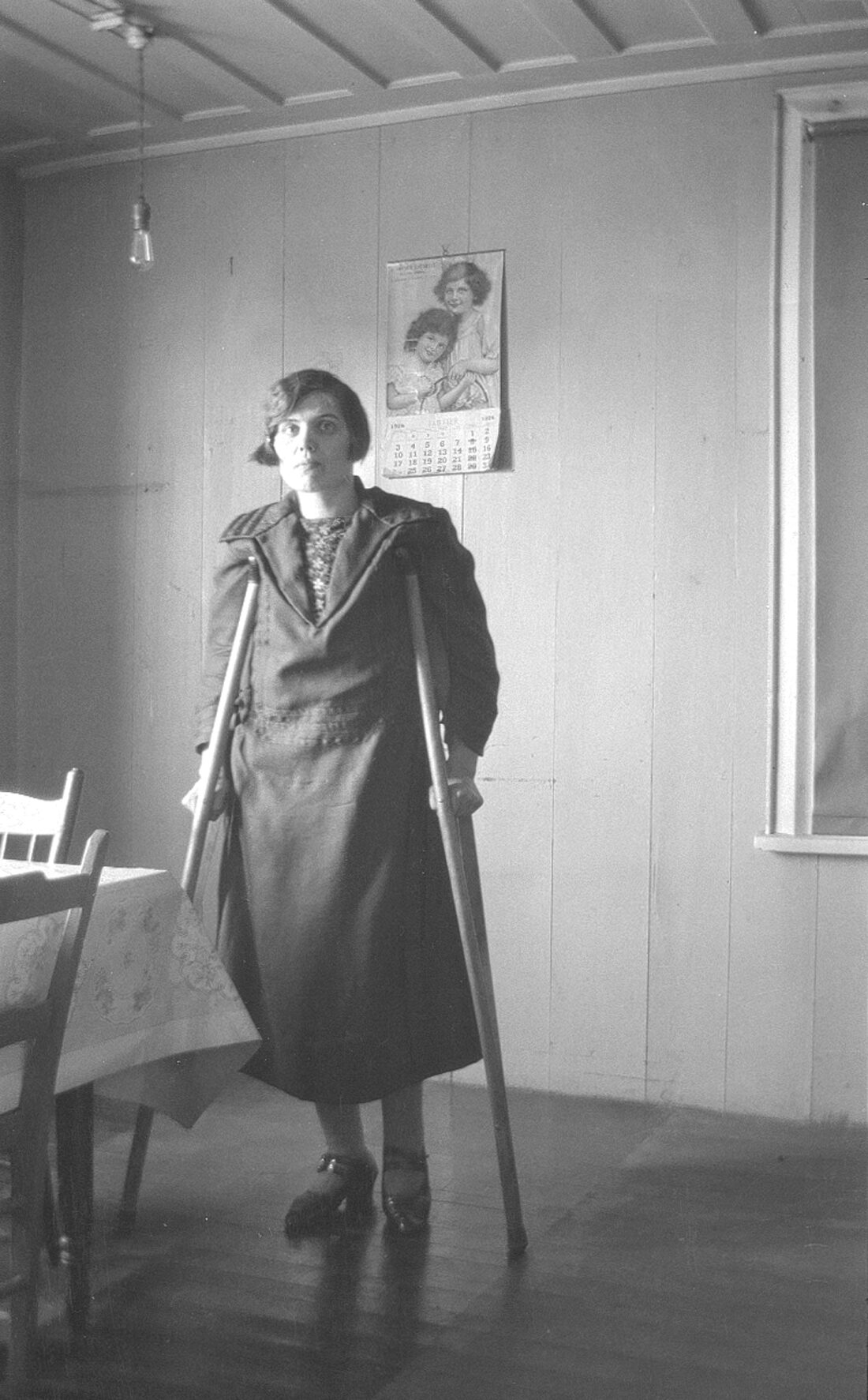 Marie-Louise Dumont âgée d'environ 30 ans, en béquilles, dans une cuisine.