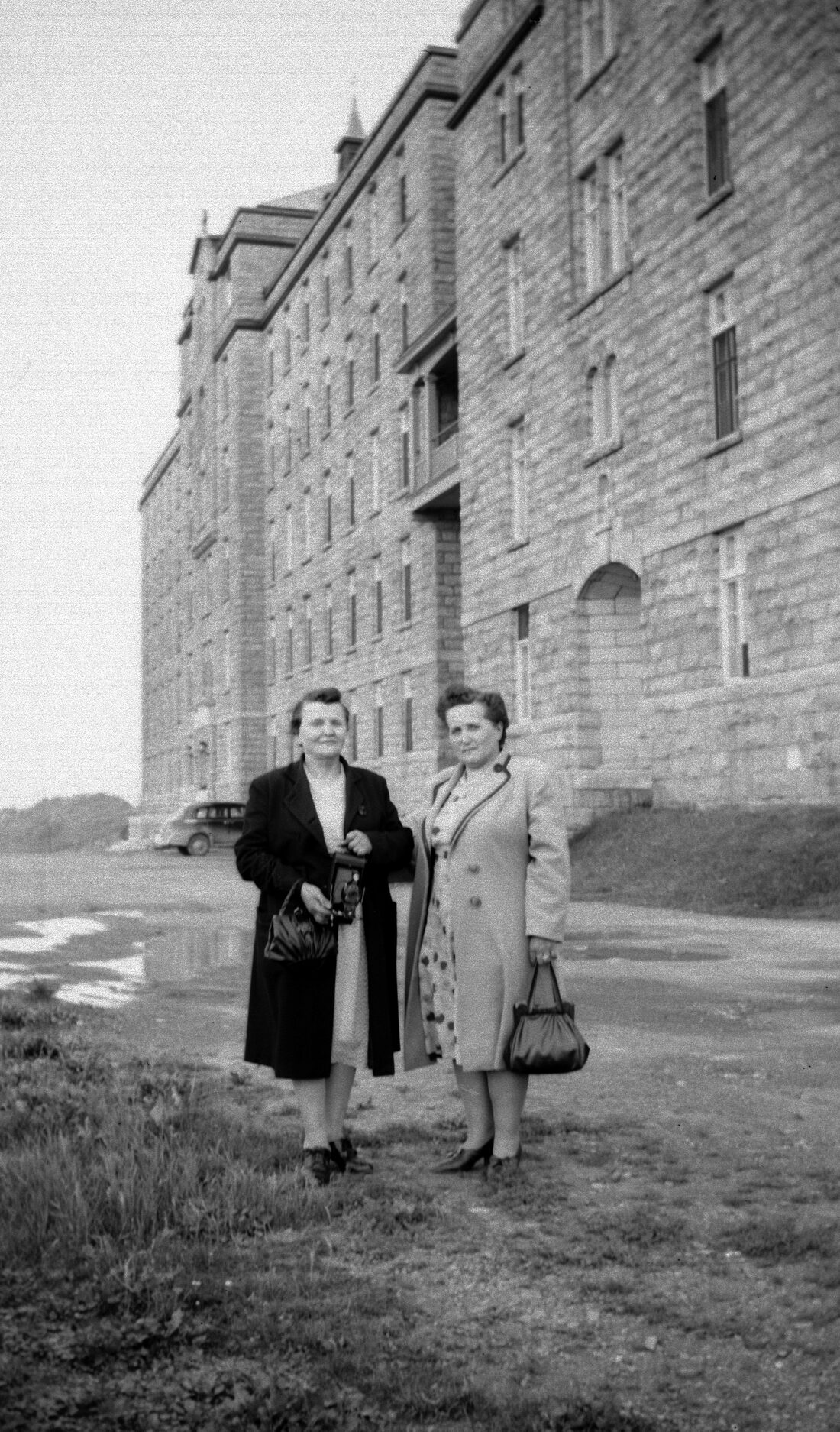 Marie-Alice Dumont et sa soeur Marie-Jeanne élégamment vêtues posant devant un grand édifice.