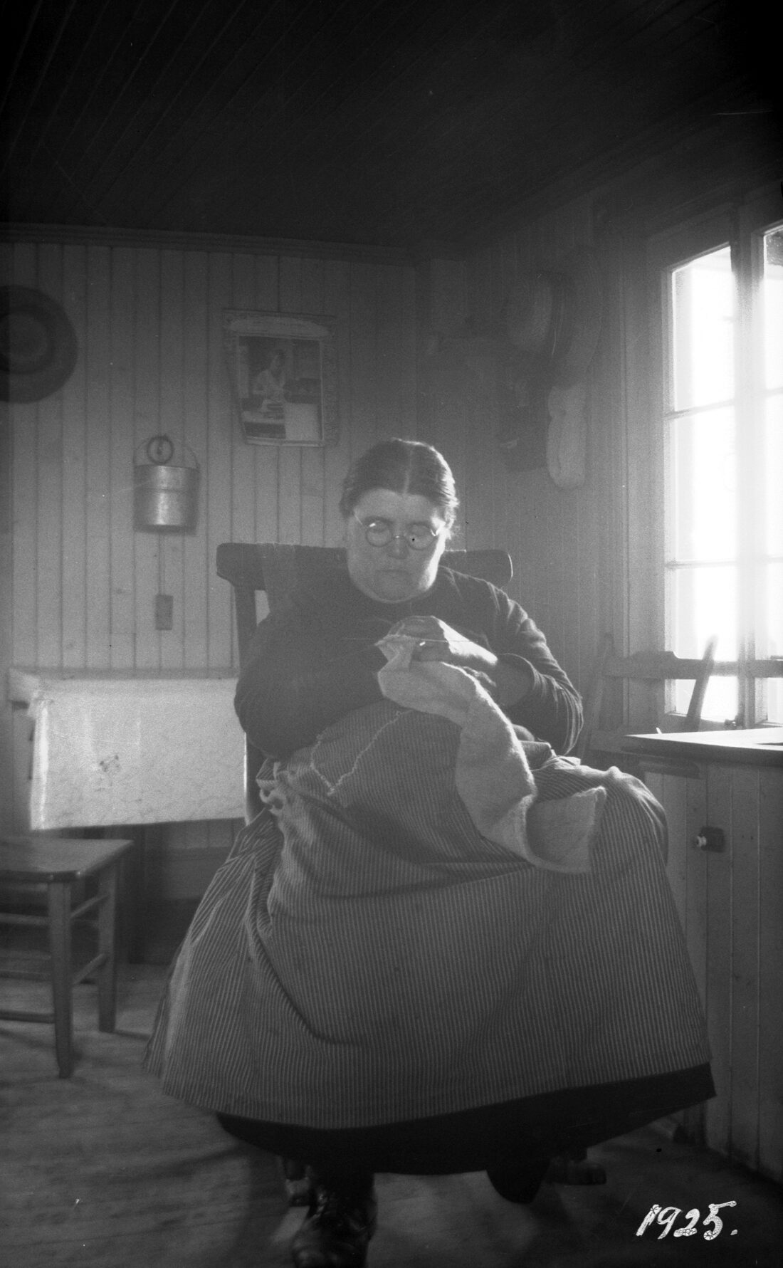 Marie Pelletier endormi sur une chaise berçante, tricot dans les mains, dans sa cuisine illuminée par la lumière du soleil.