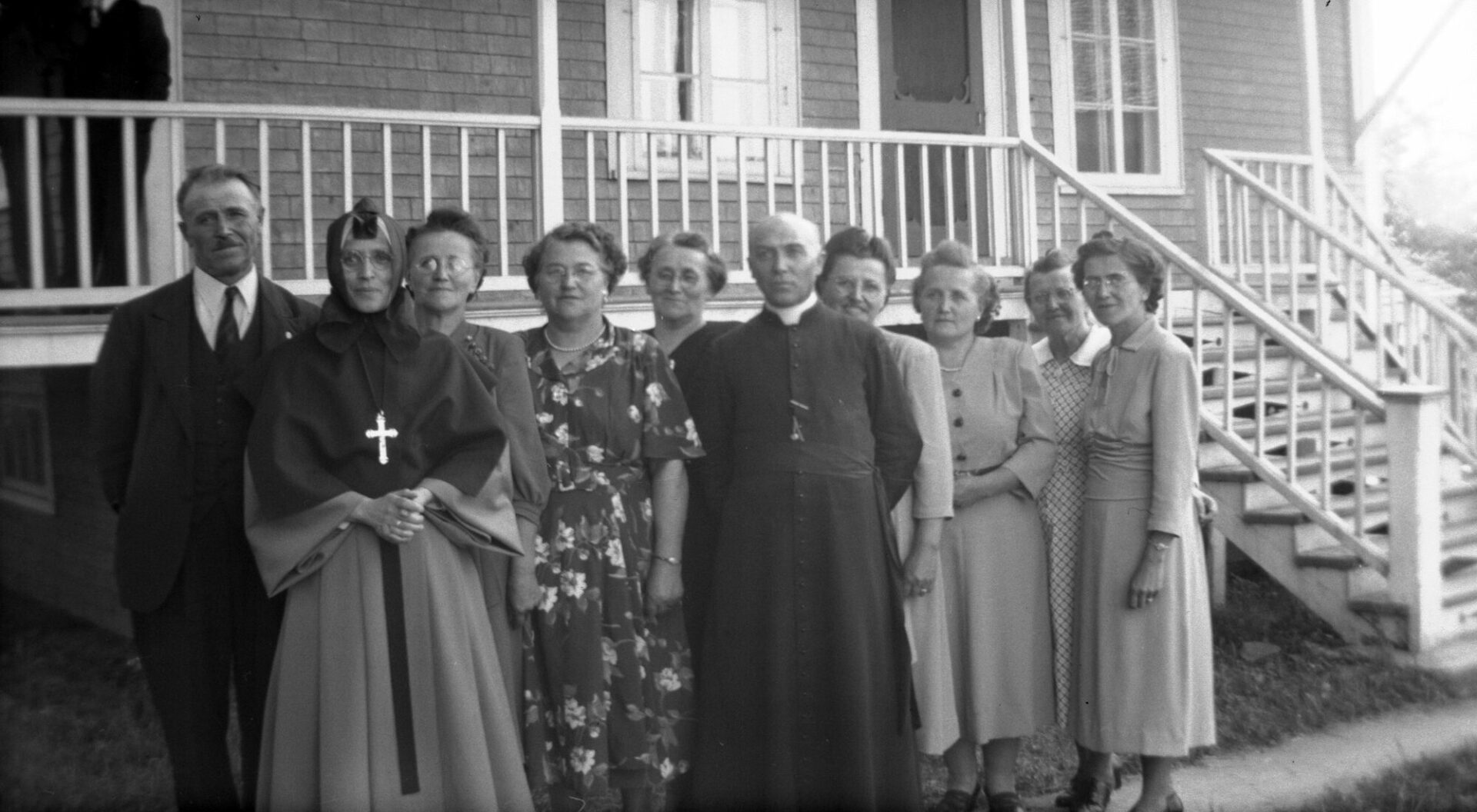 Onze membres élégamment vêtus de la fratrie des Dumont devant la galerie et le perron d'une maison.