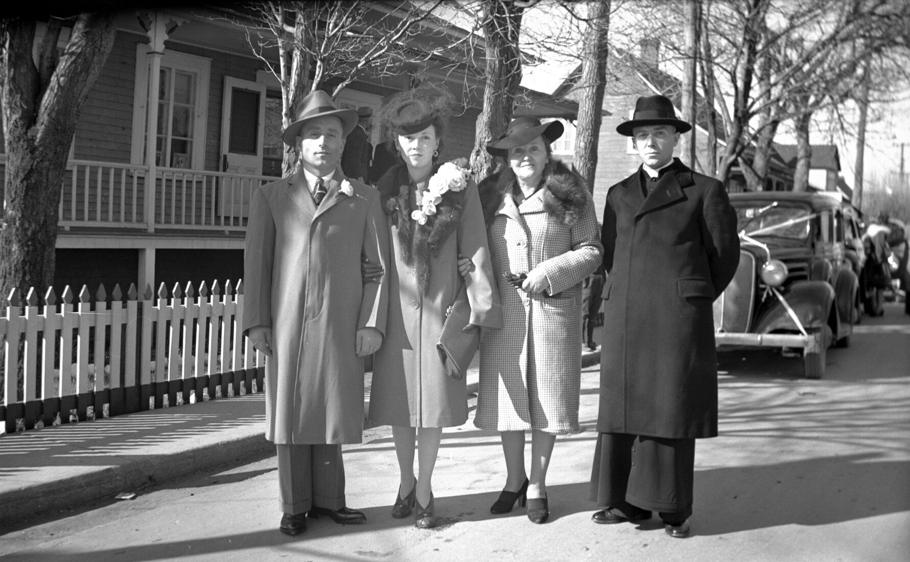 Rosalie Bergeron le jour de son mariage accompagné de son mari, de Marie-Alice et Joseph-Napoléon Dumont dans la rue en face du studio Dumont et devant un cortège de voitures décorées pour l'occasion.