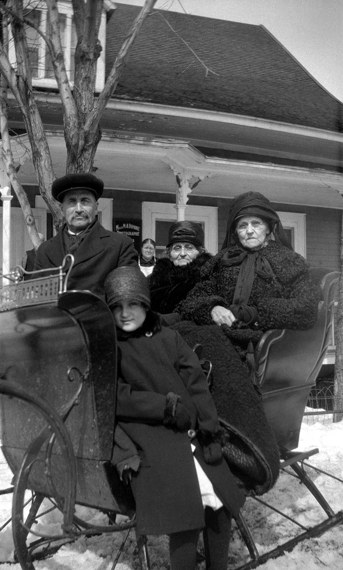 Vue rapprochée d'un groupe de quatre personnes posant, dans un traîneau, devant le studio Dumont.