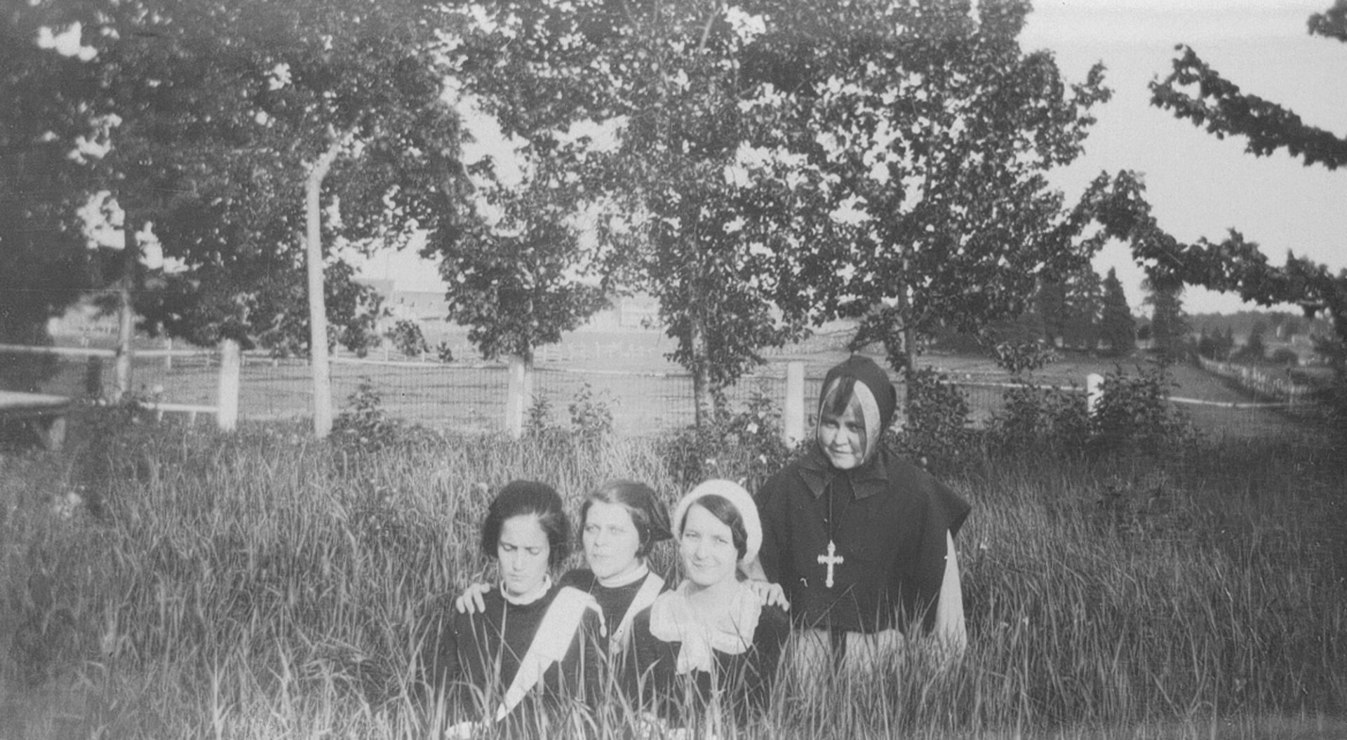 Une religieuse et trois couventines agenouillées ou assises dans l'herbe haute.