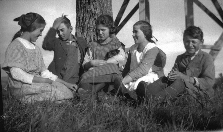 Cinq enfants âgés d'environ 10 ans, souriants, assis dans l'herbe et devant un arbre.