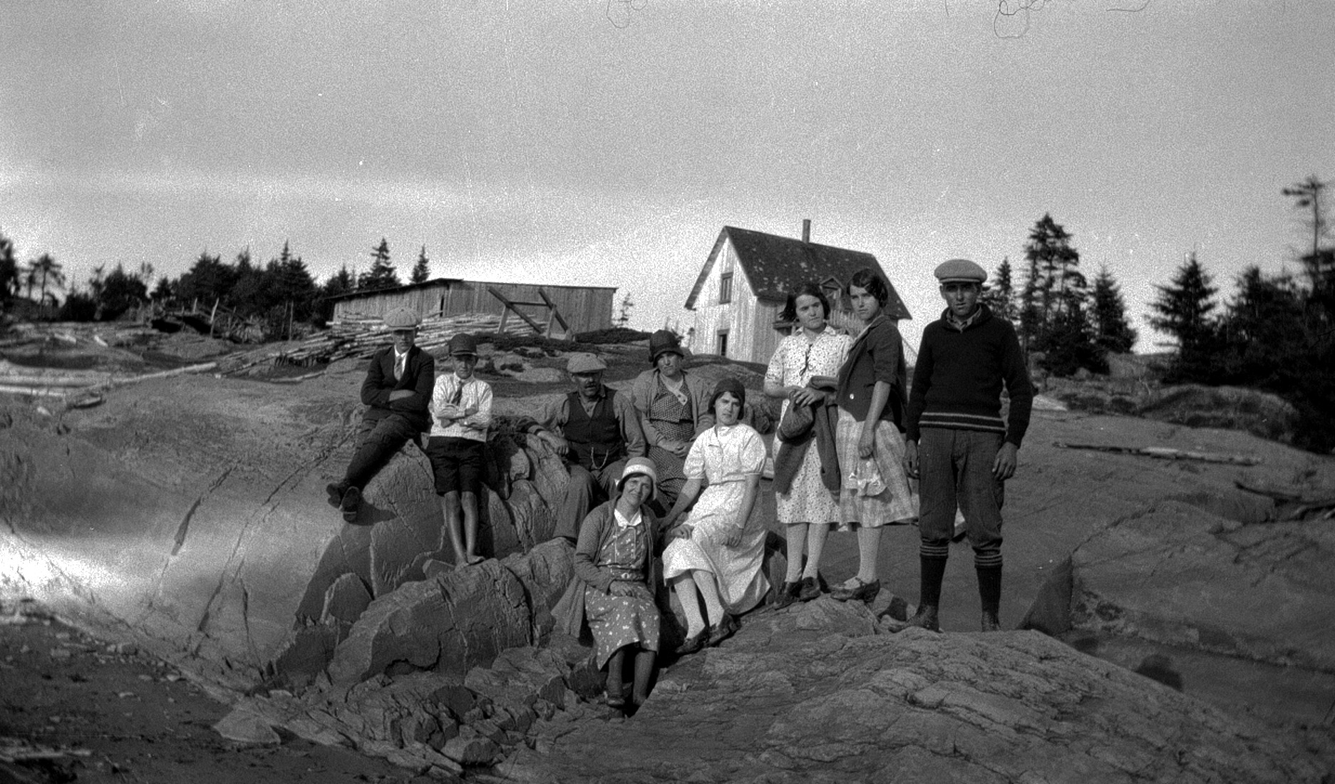 Neuf personnes posant en plein air, sur la roche, devant une maison.