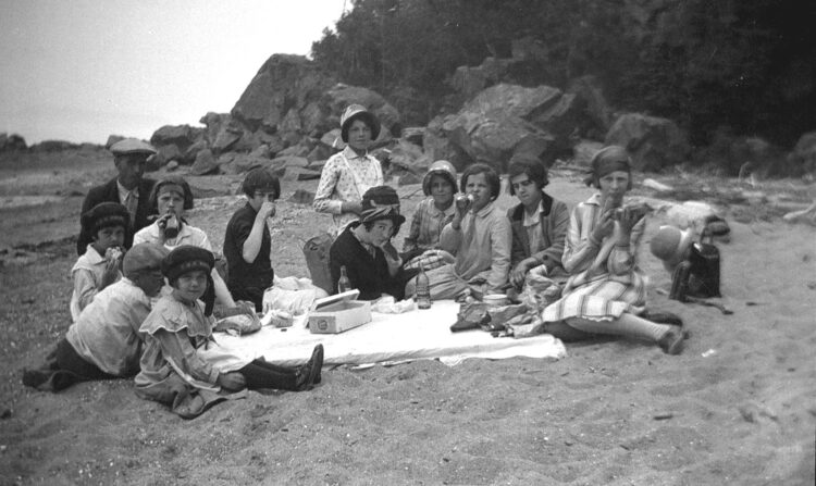 11 jeunes garçons et filles et un homme adulte pique-niquant sur la grève.