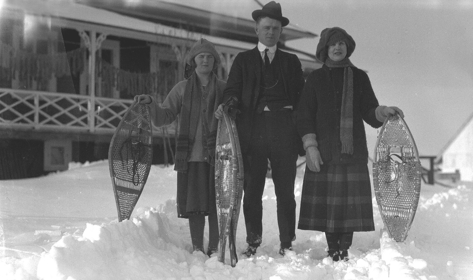 Un homme et deux jeunes femmes posant en hiver avec leurs raquettes devant une maison.