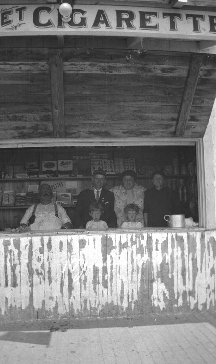 Groupe de six personnes dont deux jeunes enfants derrière le comptoir d'un kiosque vendant notamment des cigarettes.