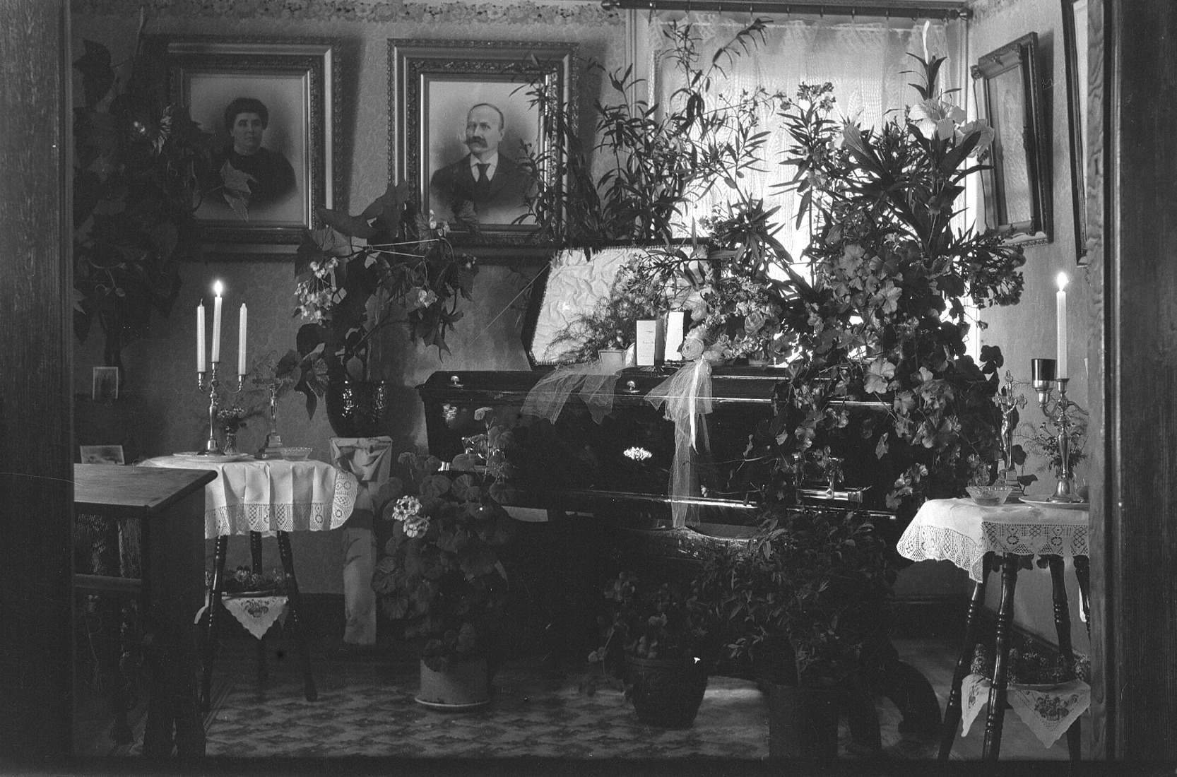 Pièce d'une maison richement décorée de plantes et de photographies et où se trouve un cercueil.
