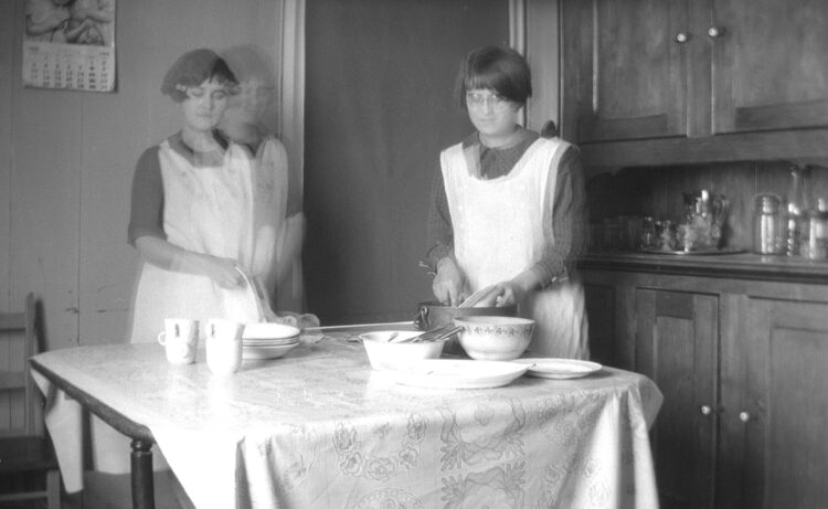 Deux adolescentes lavant et essuyant la vaisselle sur la table d'une salle à manger.