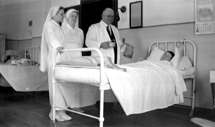 Deux gardes-malade et un médecin au soin d'une malade dans un hôpital.