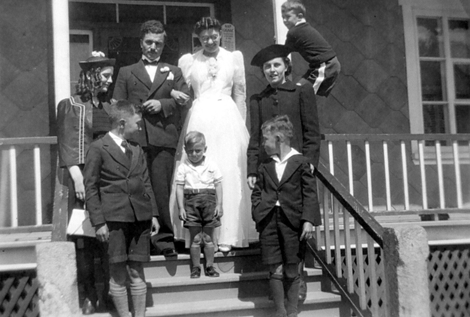 Couple de mariés et six autres personnes d'âges divers sur le perron d'une résidence.