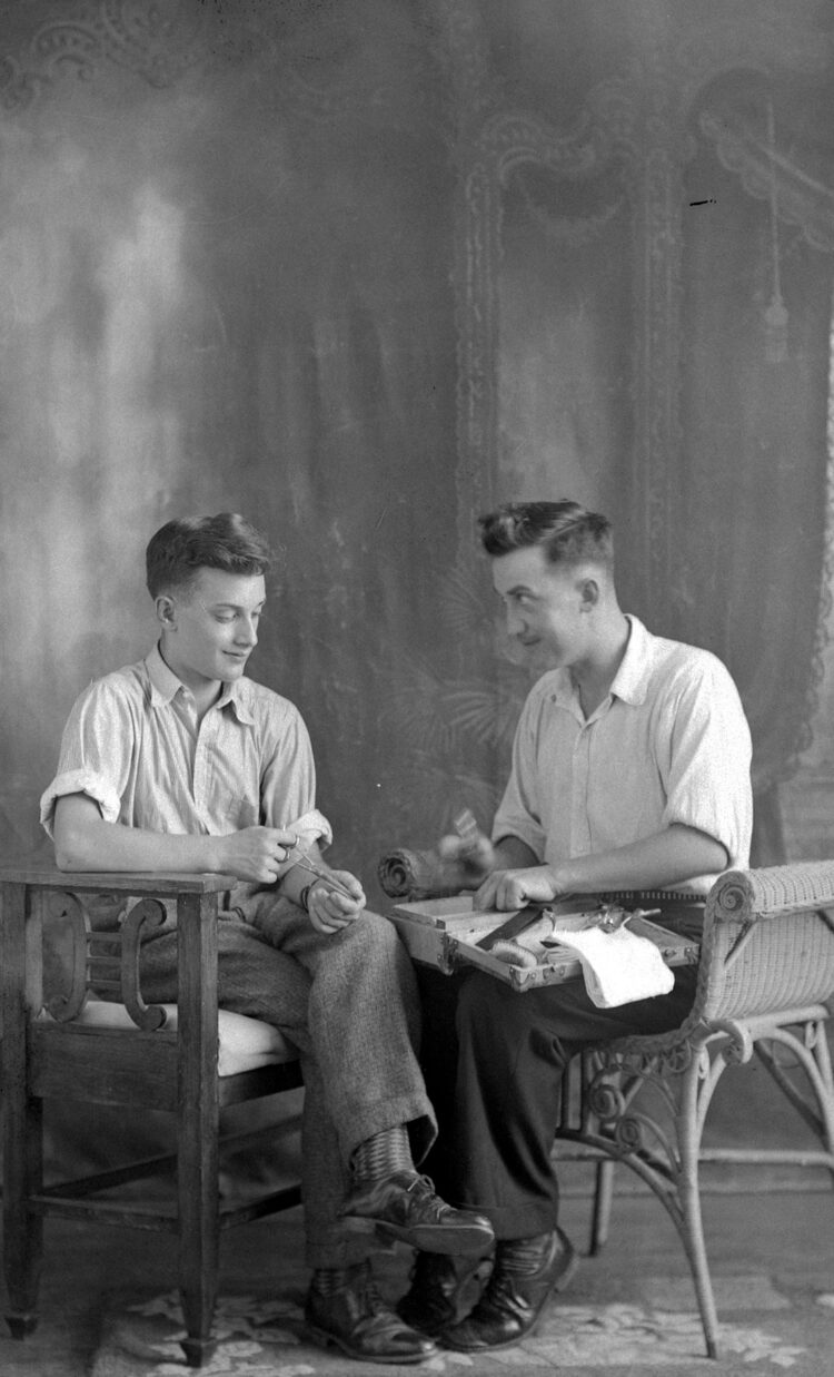 Portrait de studio d'un jeune homme avec son oncle qui lui montre des outils que contient une valise posée sur ses genoux.