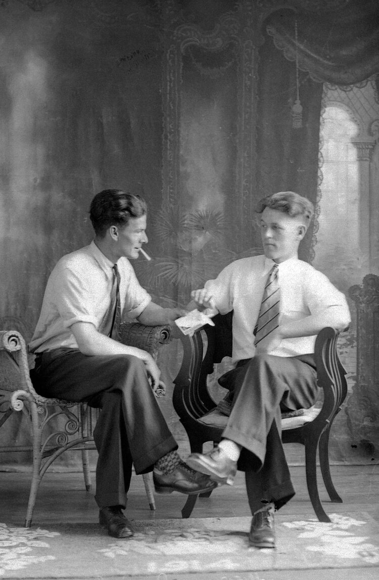 Portrait de studio de deux hommes assis et se regardant, l'un offrant une cigarette à l'autre.
