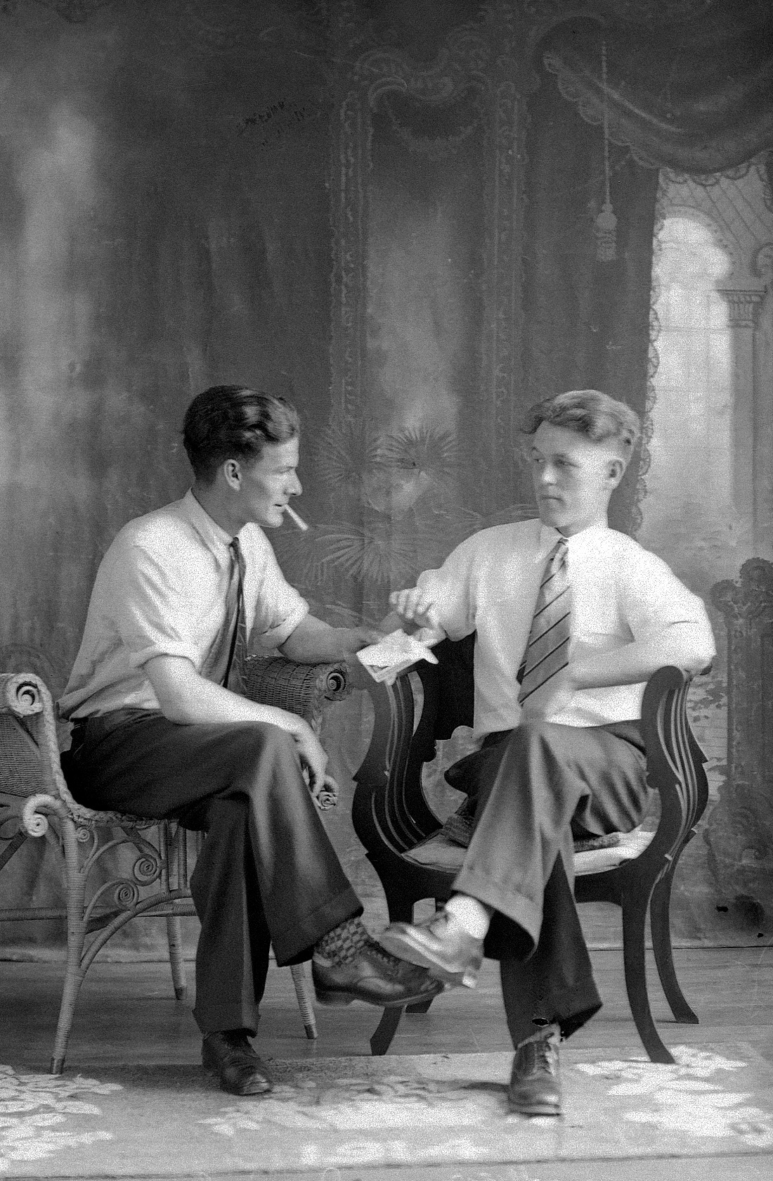 Portrait de studio de deux hommes assis et se regardant, l'un offrant une cigarette à l'autre.