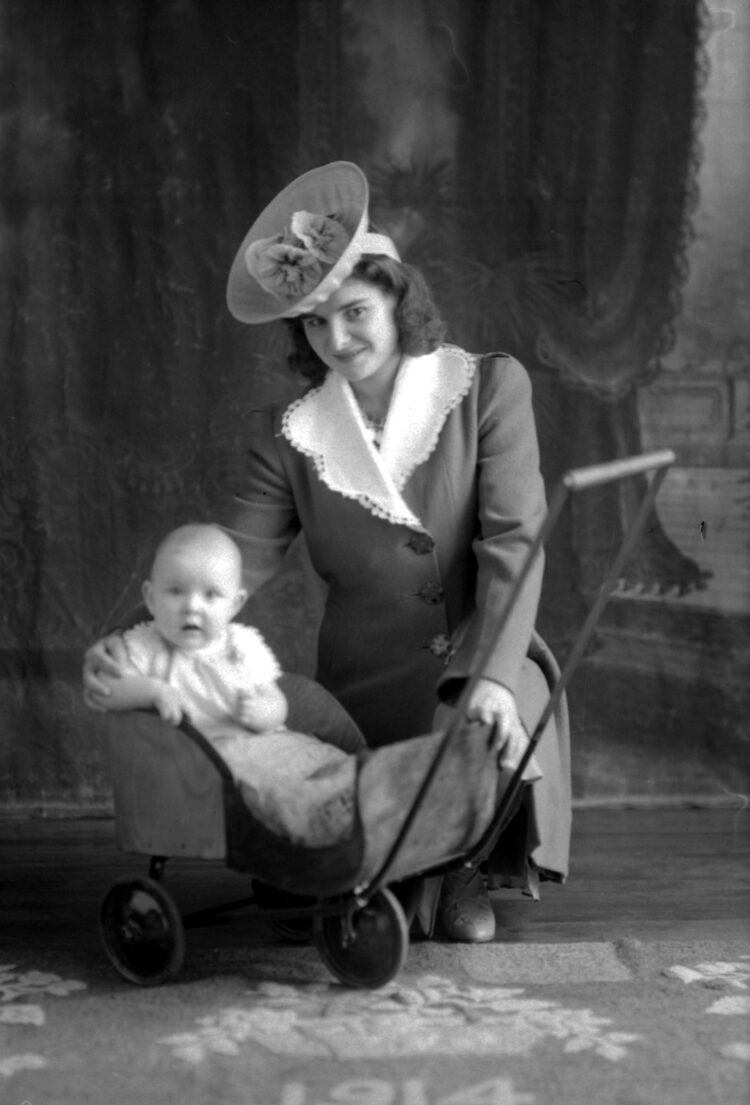 Portrait de studio d'une femme élégamment vêtue et de son bébé installé dans un petit chariot.