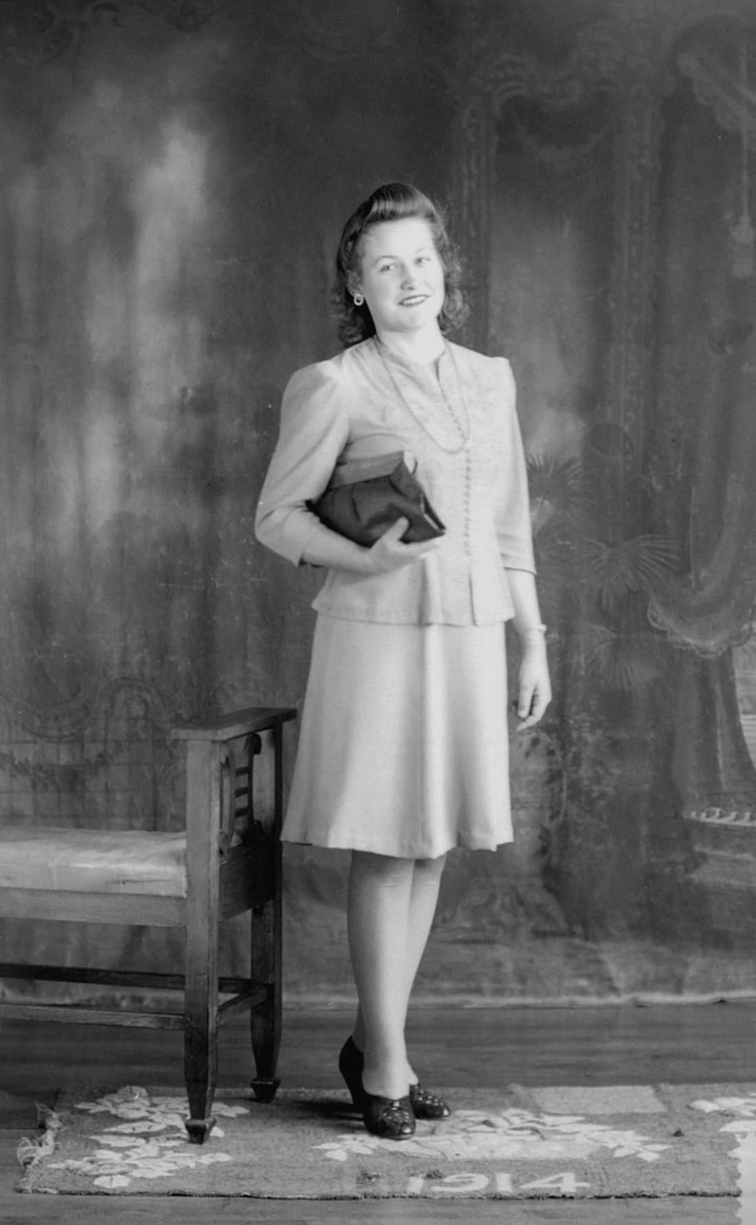 Portrait de studio d'une jeune femme élégamment vêtue et tenant une sacoche dans sa main droite.