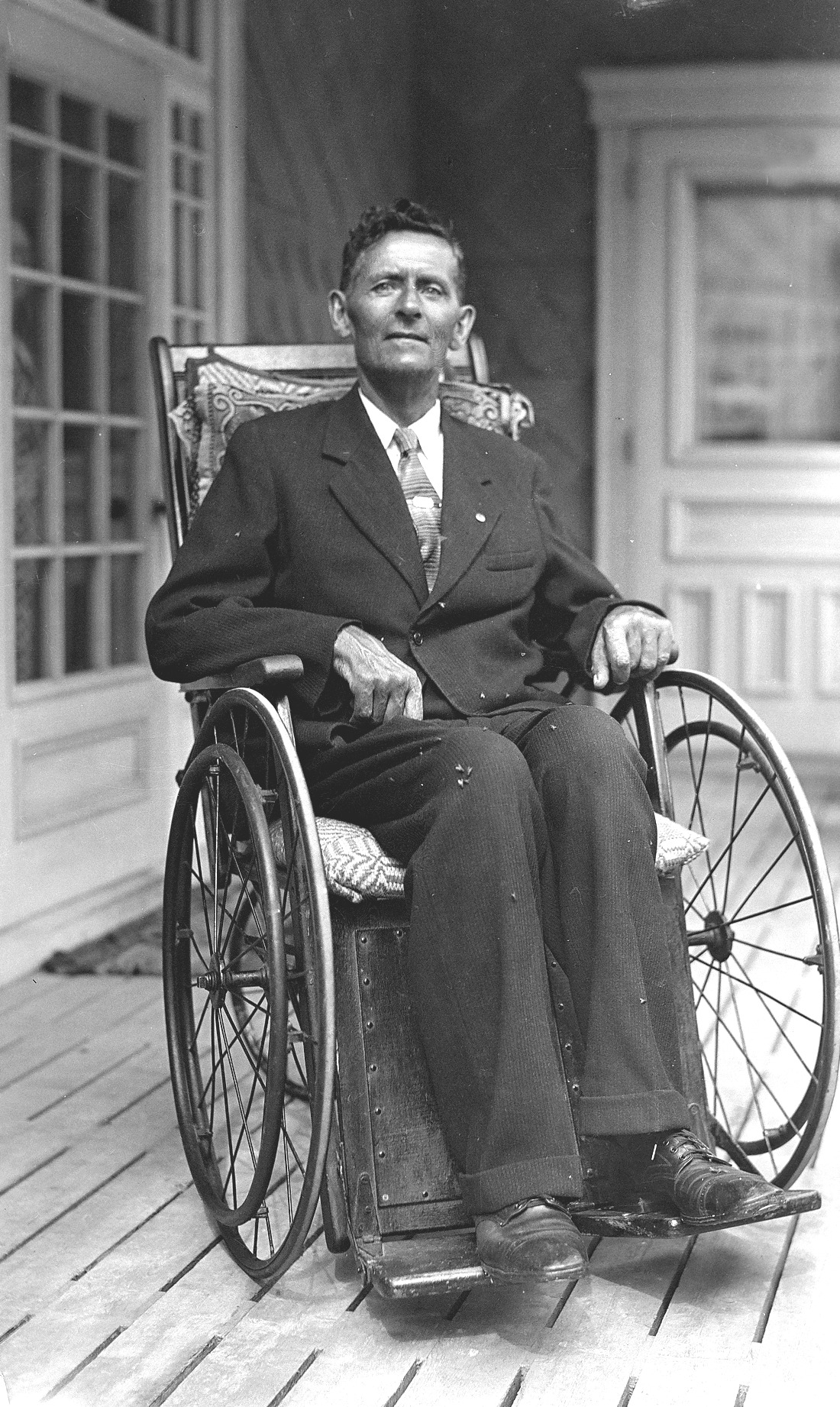 Un homme élégamment vêtu en chaise roulante sur la galerie d'une résidence.