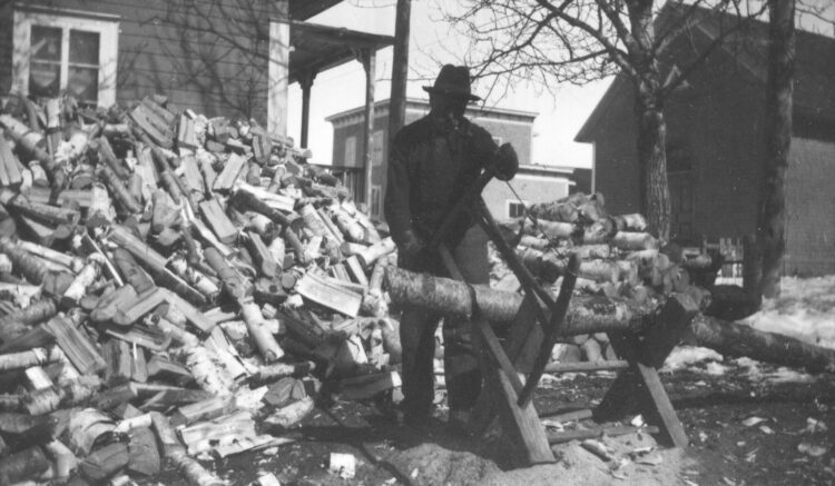 Un homme au sciage d'une grande quantité de bois dans un environnement villageois.