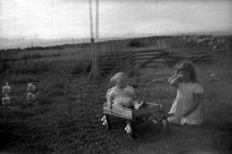 Un bébé dans un chariot et une fillette à genoux à ses côtés dans un environnement campagnard, scène reproduite avec distorsion dans ce cliché raté.