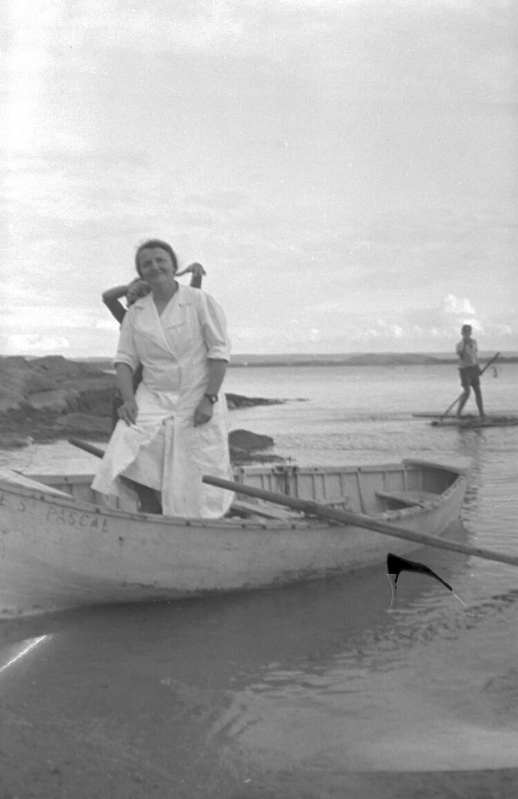 Marie-Alice Dumont en costume de bain blanc debout dans un petit bateau nommé "Le St Pascal".