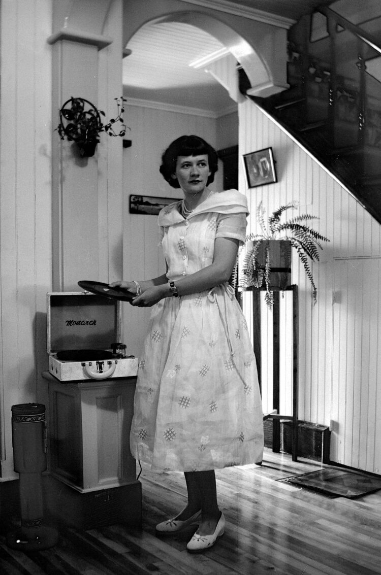 Une jeune femme élégamment vêtue dans un environnement domestique s'apprêtant à placer un disque dans un tourne-disque portable de marque "Monarch".