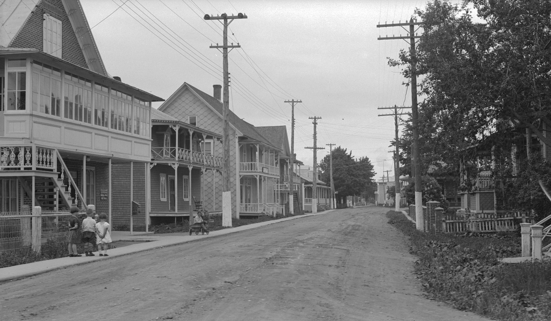 Scène de rue villageoise dans laquelle cinq enfants semblent jouer sur un trottoir.