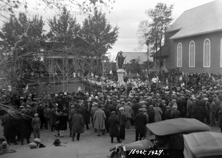 Une foule amassée près d'une église et près d'un presbytère.