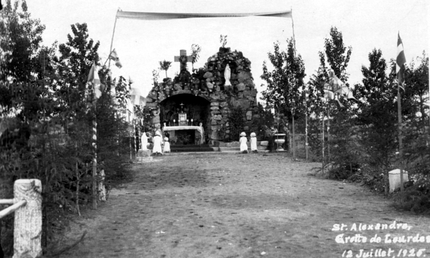 Grotte de Notre-Dame-de-Lourdes située au bout d'une allée centrale d'un cimetière et devant laquelle sont agenouillées quatre jeunes enfants.