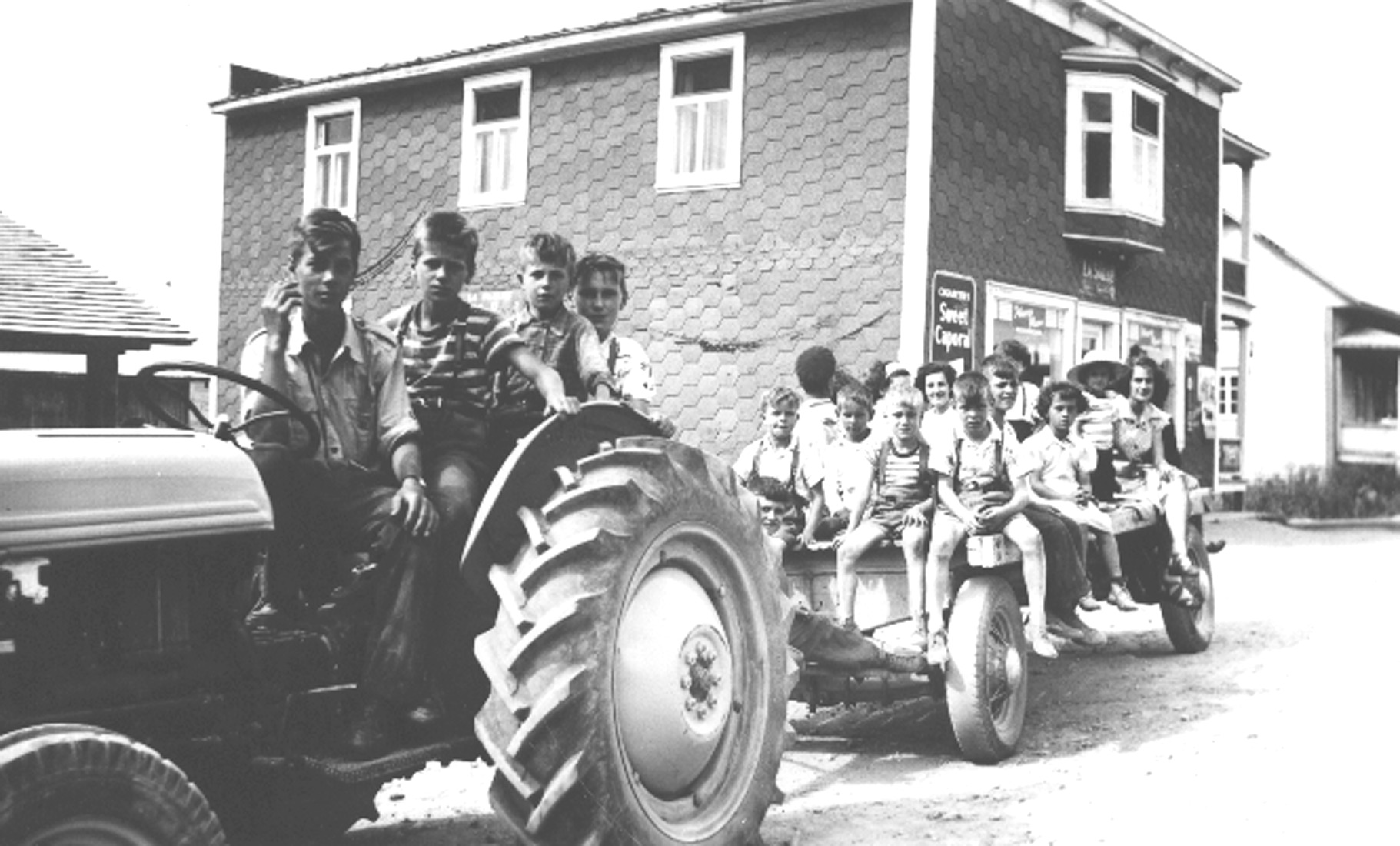 Quatre jeunes garçons sur un tracteur tirant un wagon sur lequel sont assis une quinzaine de garçons et filles.