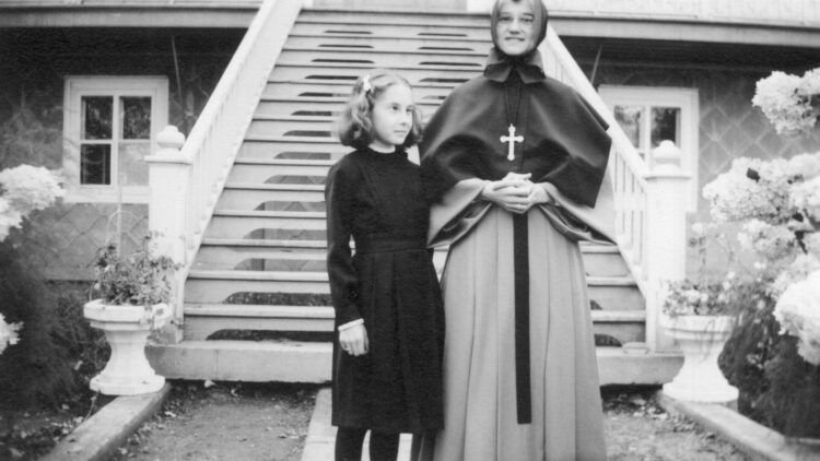 Une religieuse et une couventine qui semble aveugle debout, à l'extérieur, devant les grands escaliers d'un couvent.