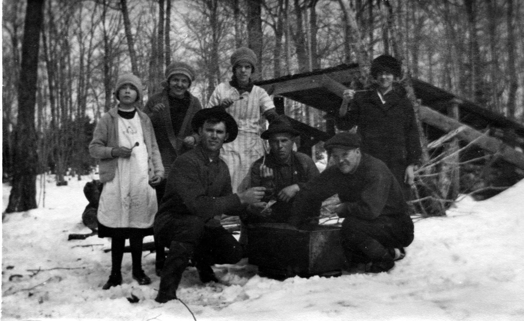 Un groupe de sept personnes d'âges variés, à l'extérieur, à la cabane à sucre et mangeant de la tire d'érable.