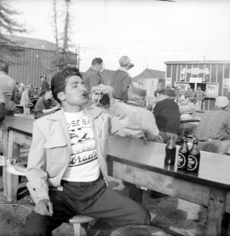 Jeune homme attablé et buvant une bière lors d'un événement en plein air.