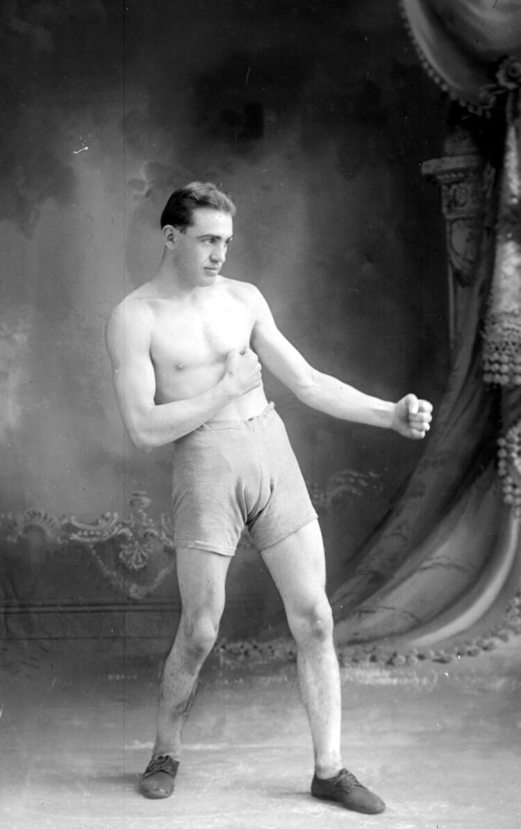 Portrait en studio d'un homme torse nu et en shorts simulant les poings fermés un combat de boxe.