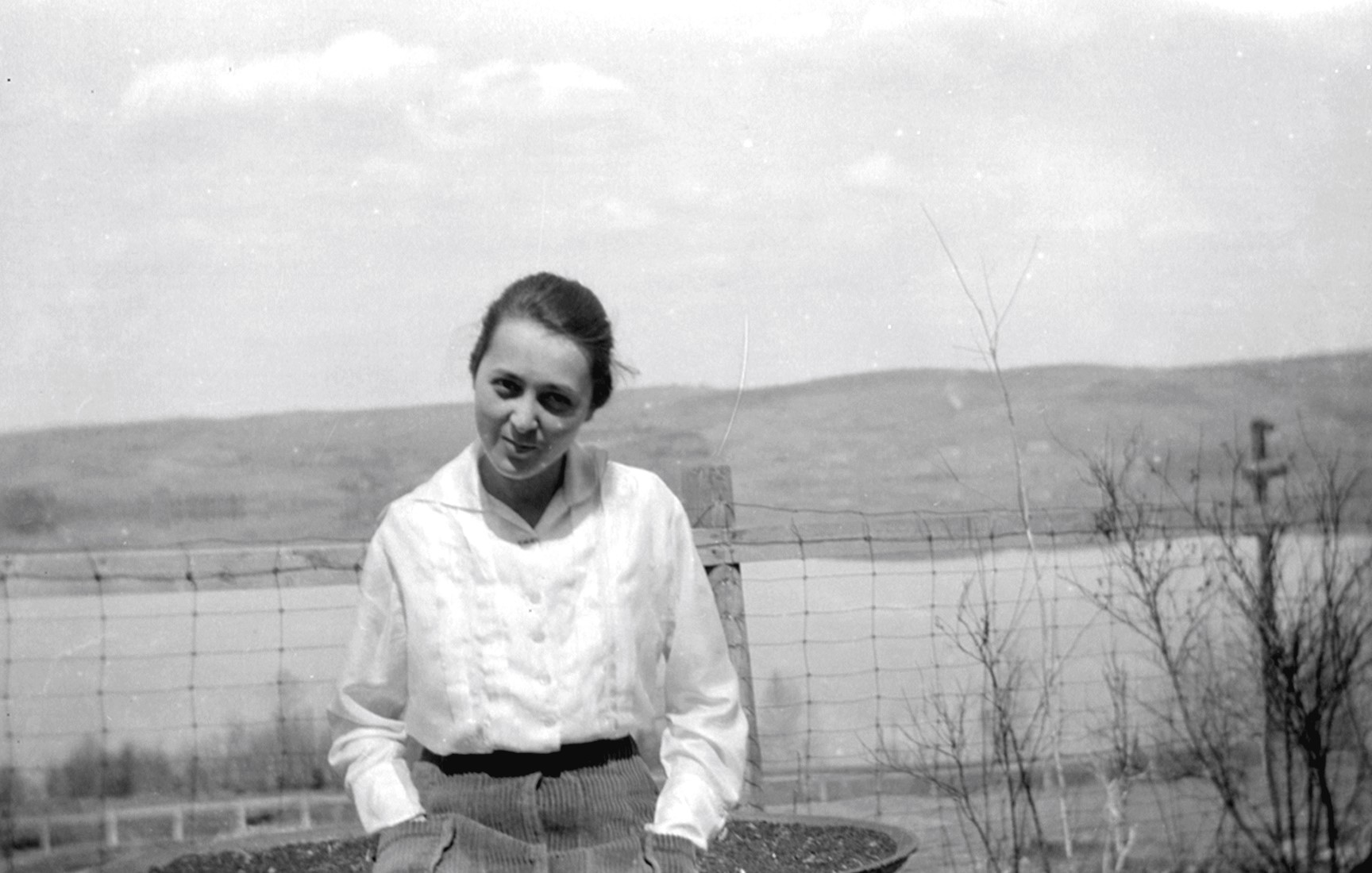 Portrait d'Aline Cloutier âgée d'environ 15 ans avec en arrière-plan un lac et des collines.