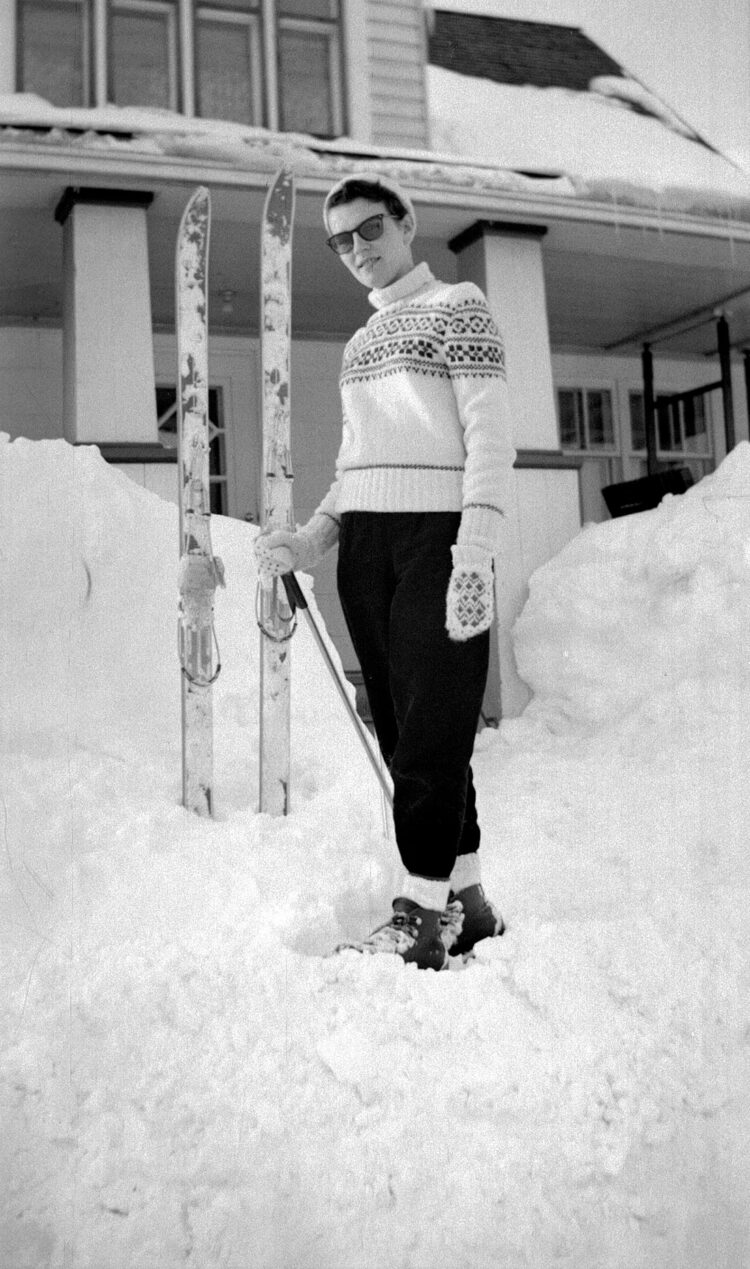 Jeune femme posant devant une maison, en hiver, avec ses skis.