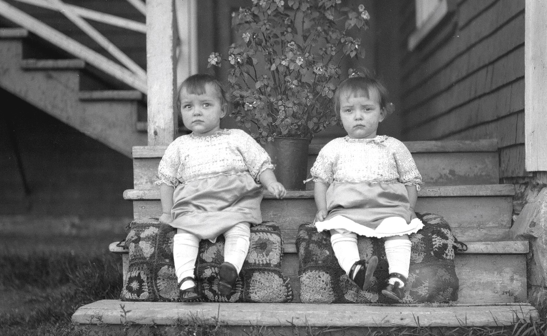 Portrait de deux jumelles âgées d'environ deux ans assises sur le perron de la maison de la famille Dumont.
