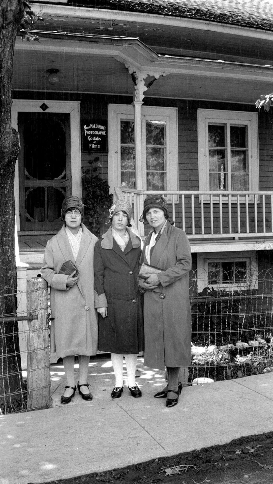 Marie-Alice et Elizabeth Dumont avec Rosalie Bergeron devant le studio Dumont, une affiche indique "Melle M. A. Dumont Photographe Kodaks et Films".