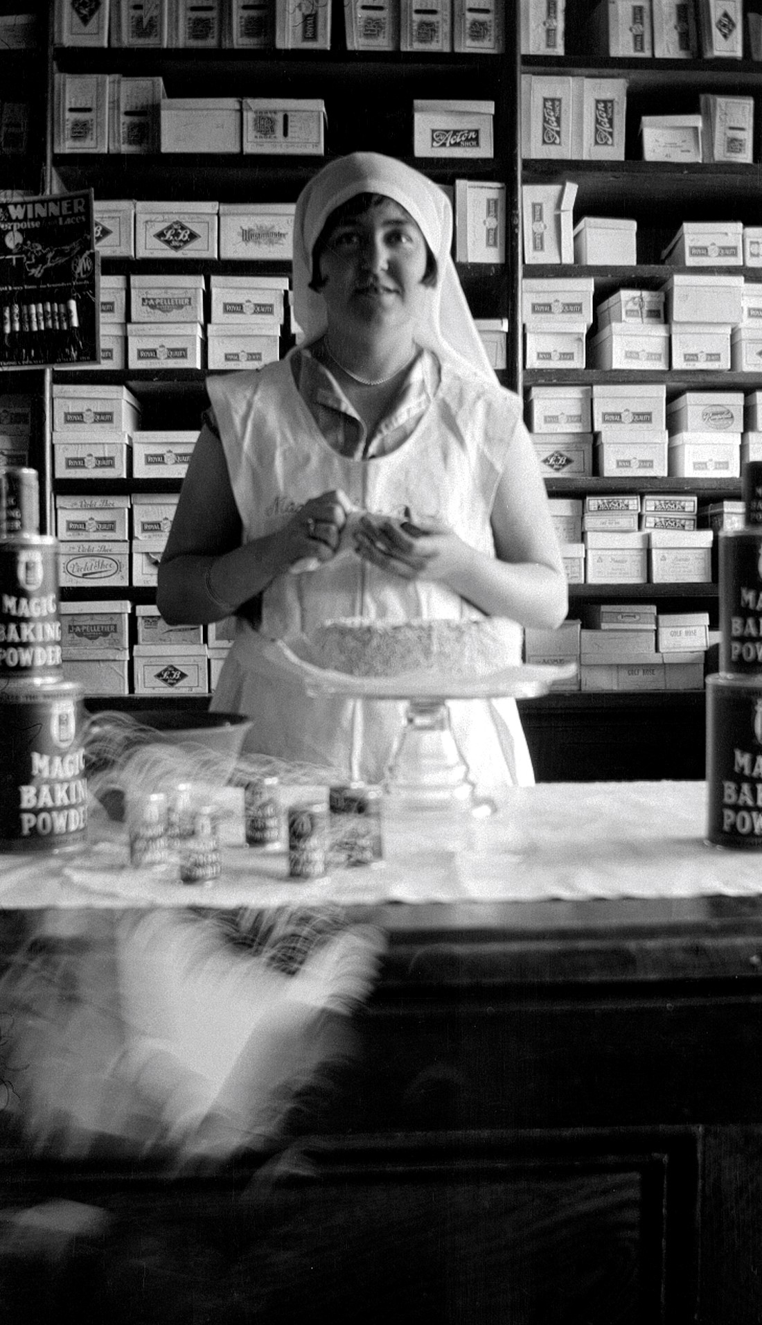 Jeune femme au comptoir d'un magasin général en habits de pâtissière et préparant un gâteau.