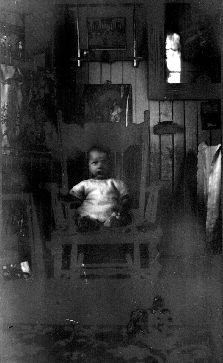 Un bébé sur une chaise berçante dans un environnement domestique sur un cliché trop sombre.